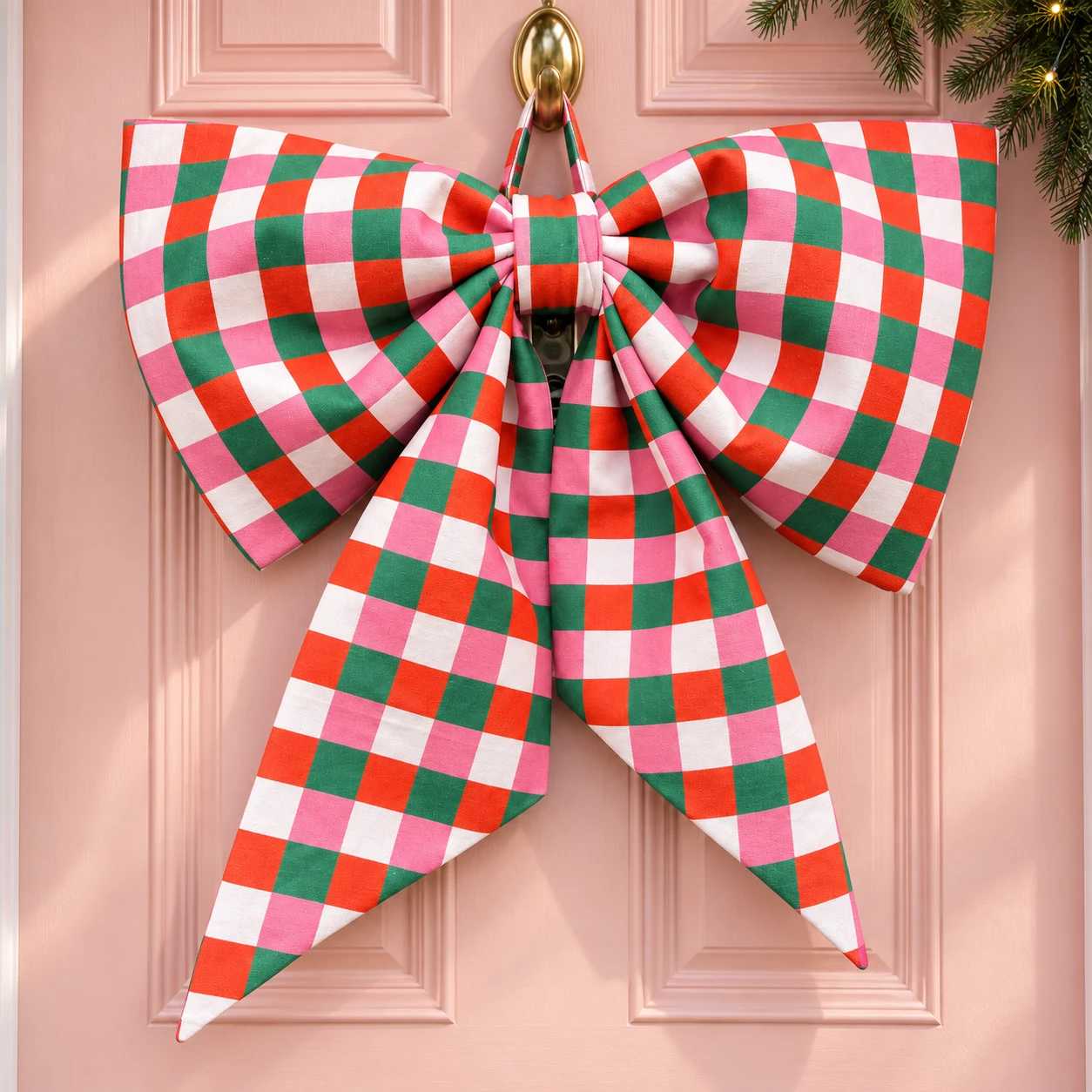Oversized red, pink and green checked Christmas bow on a pink front door — styled concept image